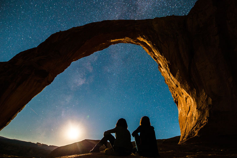 Two people sitting under a stone arch at night